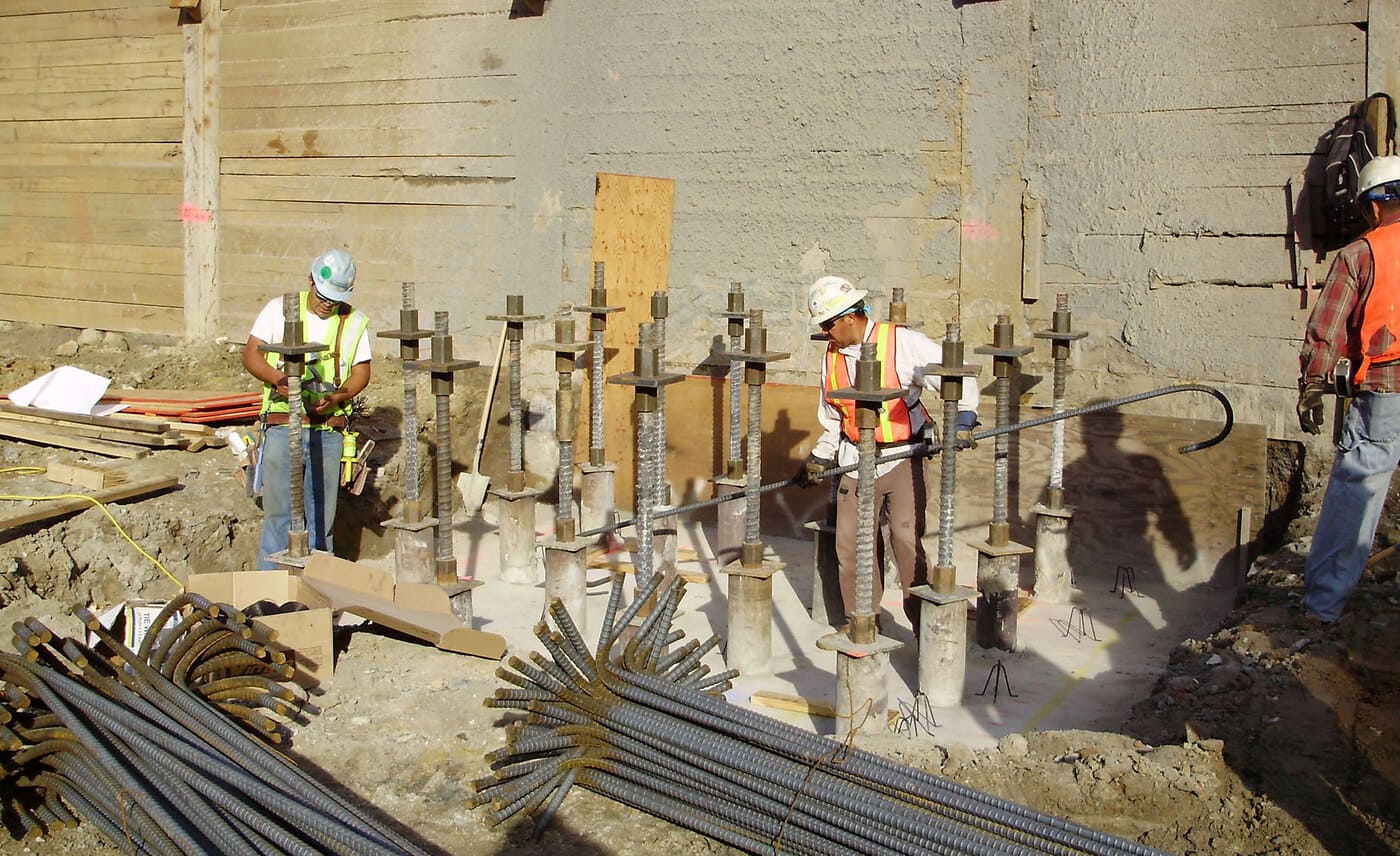 Construction workers setting micropiles up next to retaining wall on job site